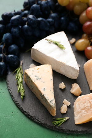 Slate plate with cheese and ripe juicy grapes on color tableの写真素材