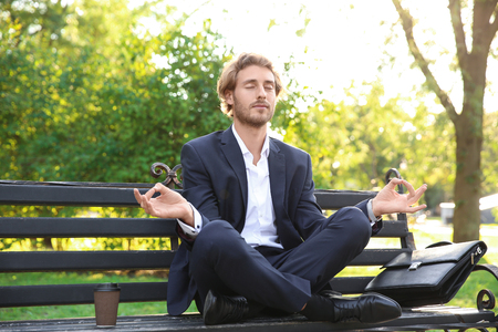 Handsome young businessman meditating on bench in parkの写真素材