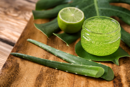 Jar with aloe vera gel and tropical leaf on wooden boardの写真素材
