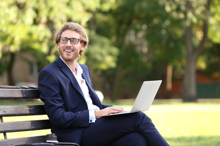 Handsome young businessman with laptop resting on bench in parkの写真素材