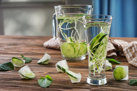 Glass and jug of fresh cucumber water on wooden tableの写真素材