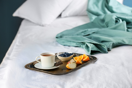 Metal tray with delicious breakfast on bed