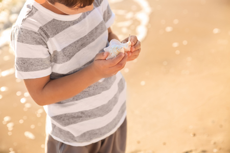 Cute little boy with sea shell on beach, closeupの写真素材