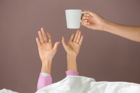 Giving of hot coffee to sleepy woman under blanket in bedの写真素材