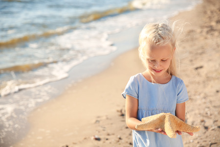 Cute little girl with starfish on sea beachの写真素材