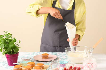 Woman preparing cream for delicious cupcakes at tableの写真素材