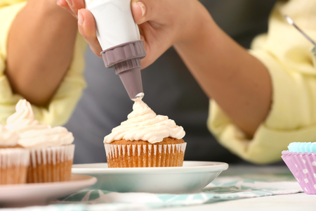 Woman decorating delicious cupcake with cream at table, closeupの写真素材