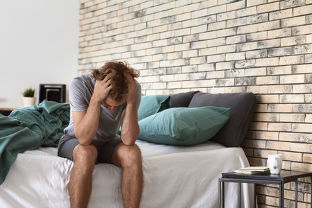 Depressed young man sitting on bedの写真素材