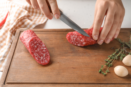 Woman cutting delicious smoked sausage on wooden boardの写真素材
