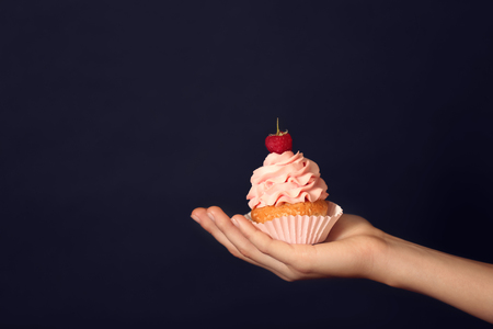 Female hand holding delicious cupcake on dark backgroundの写真素材