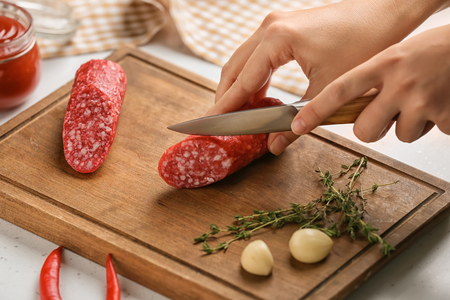 Woman cutting delicious smoked sausage on wooden boardの写真素材