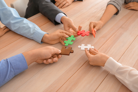 Business team assembling puzzle on wooden tableの写真素材