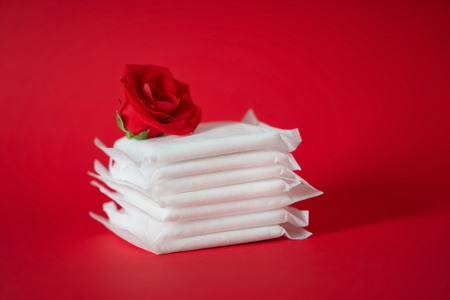 Stack of menstrual pads with red rose on color backgroundの写真素材
