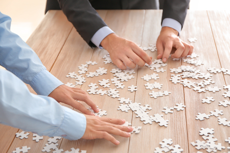 Business team assembling puzzle on wooden tableの写真素材