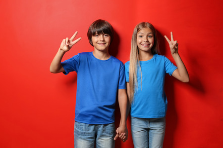 Boy and girl in t-shirts showing Victory gesture on color backgroundの写真素材