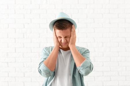 Portrait of handsome stressed young man against white brick wall