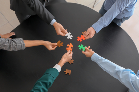 Business team assembling puzzle on dark tableの写真素材