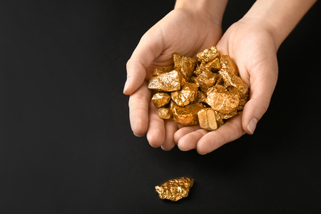 Female hands with gold nuggets on black backgroundの写真素材