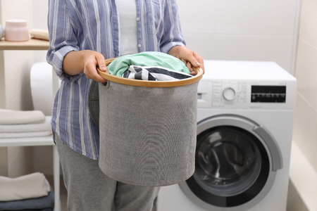 Woman holding laundry basket with dirty clothes in bathroomの写真素材