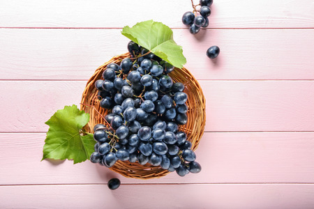 Wicker plate with ripe sweet grapes on color wooden table, top viewの写真素材