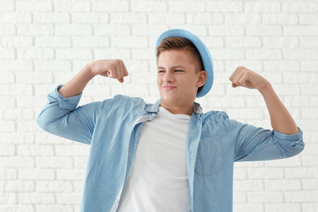 Portrait of handsome young man showing muscles against white brick wallの写真素材