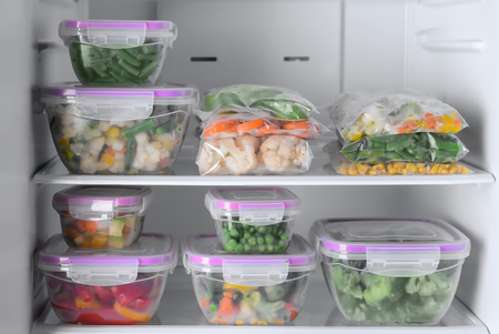 Containers and plastic bags with frozen vegetables in refrigeratorの写真素材