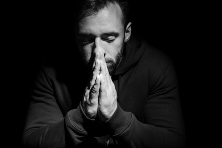 Religious young man praying to God on dark background, black and white effectの写真素材