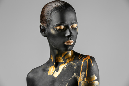 Beautiful woman with black and golden paint on her body against light backgroundの写真素材
