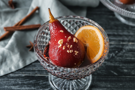 Glass bowl with delicious poached pear in red wine on wooden tableの写真素材