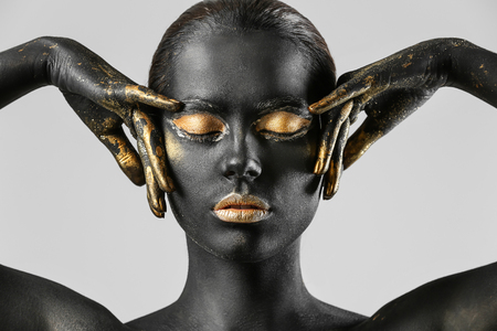 Beautiful woman with black and golden paint on her body against light backgroundの写真素材