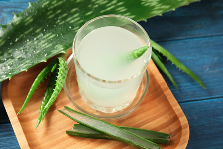 Wooden tray with glass of fresh aloe vera juice and leaves on tableの写真素材