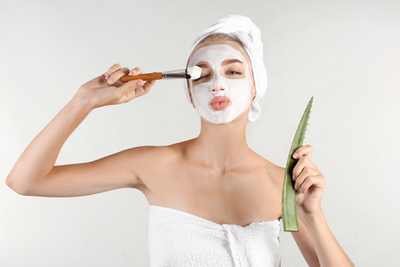 Beautiful young woman with facial mask containing aloe vera extract, on light backgroundの写真素材