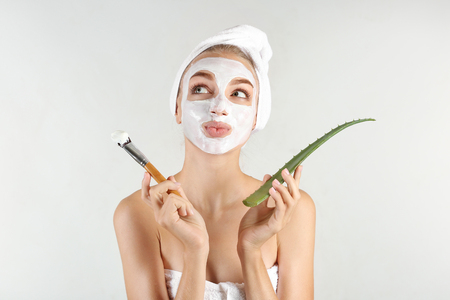 Beautiful young woman with facial mask containing aloe vera extract, on light backgroundの写真素材