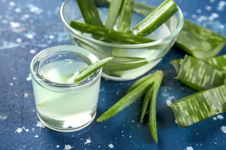 Glassware with fresh aloe vera juice and leaves on color tableの写真素材