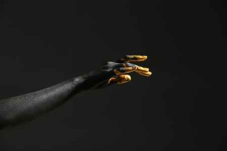 Hand of woman with black and golden paint on her skin against dark backgroundの写真素材