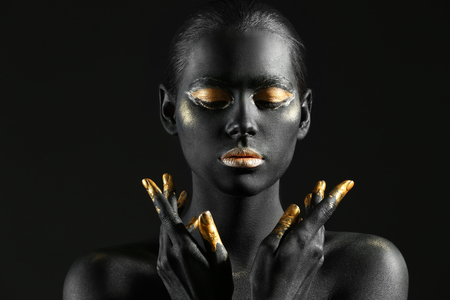 Beautiful woman with black and golden paint on her body against dark backgroundの写真素材