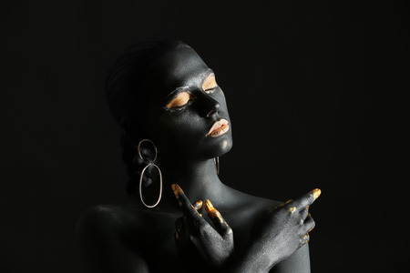 Beautiful woman with black and golden paint on her body against dark backgroundの写真素材