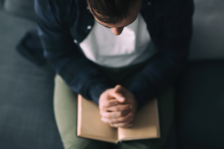 Religious young man with Bible praying at homeの写真素材