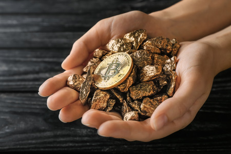 Female hands with gold nuggets and bitcoin on dark wooden background
