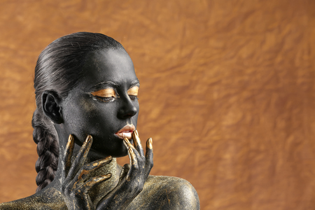 Beautiful woman with black and golden paint on her body against color backgroundの写真素材