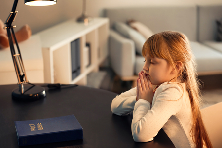 Little girl praying at dark tableの写真素材