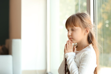 Little girl praying near window at homeの写真素材