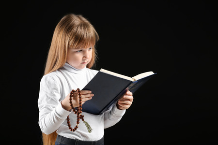Little girl reading Bible on dark backgroundの写真素材