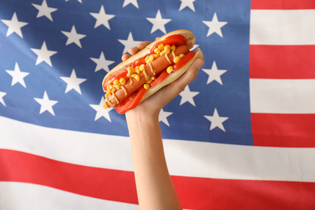 Woman holding tasty hot dog against USA flagの写真素材