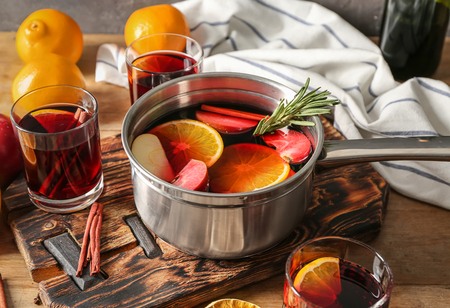 Glasses and saucepan of delicious mulled wine on wooden tableの写真素材