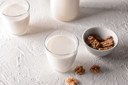 Glass of tasty milk and bowl with walnuts on white tableの写真素材