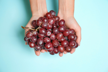 Female hands with ripe tasty grapes on color background