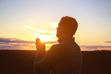 Religious man praying outdoors at sunset