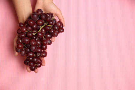 Ripe tasty grapes in female hands on color background