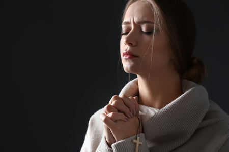 Beautiful young woman praying on dark background